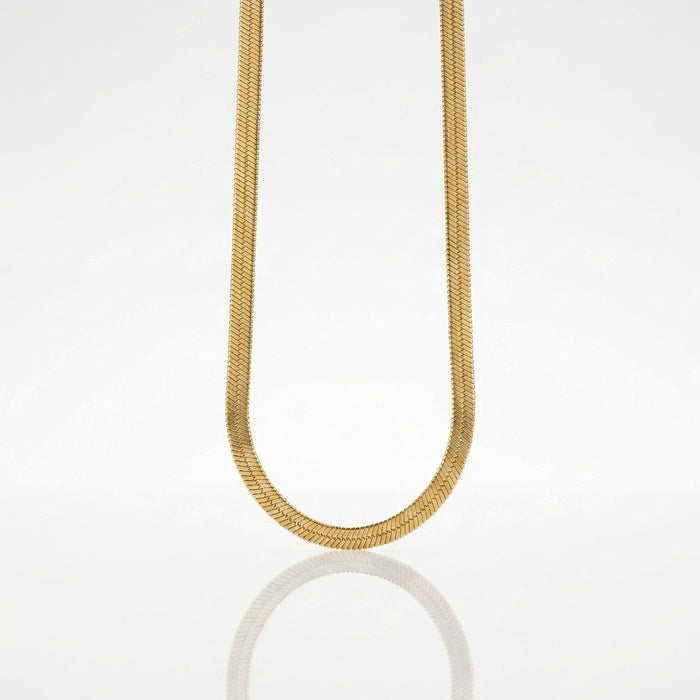 A gold snake chain necklace suspended in a U-shape against a clean white background with a soft reflection below.
