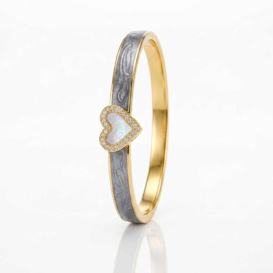A gold bangle ring featuring a textured gray inlay and a central heart-shaped opal inlay bordered by small pavé diamonds, set against a clean white background.