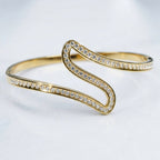 A gold S-shaped cuff bracelet adorned with pavé-set clear crystals, photographed on a clean white background.