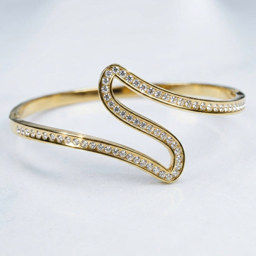A gold S-shaped cuff bracelet adorned with pavé-set clear crystals, photographed on a clean white background.