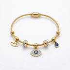 A gold cable chain bracelet with multiple charms, including an evil eye pendant, a teardrop charm with a dark blue stone, and two bezel-set clear crystal charms, displayed on a clean white background.