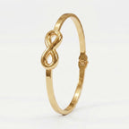 A polished gold bangle bracelet featuring a central infinity symbol, set against a clean white background.