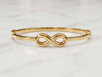 A polished gold bangle bracelet featuring a central infinity symbol