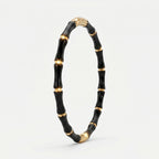 A black and gold bamboo-style bangle bracelet, standing upright on a clean white background.