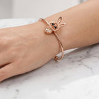 A close-up of a person's hand resting on a white marble surface, wearing a rose gold open cuff bracelet with a bunny head charm and a matching rose gold ring.