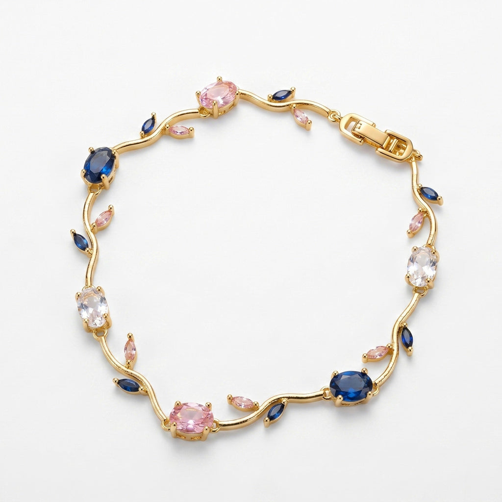 A gold vine-style bracelet featuring round pink and oval blue gemstones, clear round stones, and small marquise-cut pink accents, displayed on a clean white background.