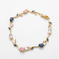 A gold vine-style bracelet featuring round pink and oval blue gemstones, clear round stones, and small marquise-cut pink accents, displayed on a clean white background.