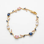 A gold vine-style bracelet featuring round pink and oval blue gemstones, clear round stones, and small marquise-cut pink accents, displayed on a clean white background.