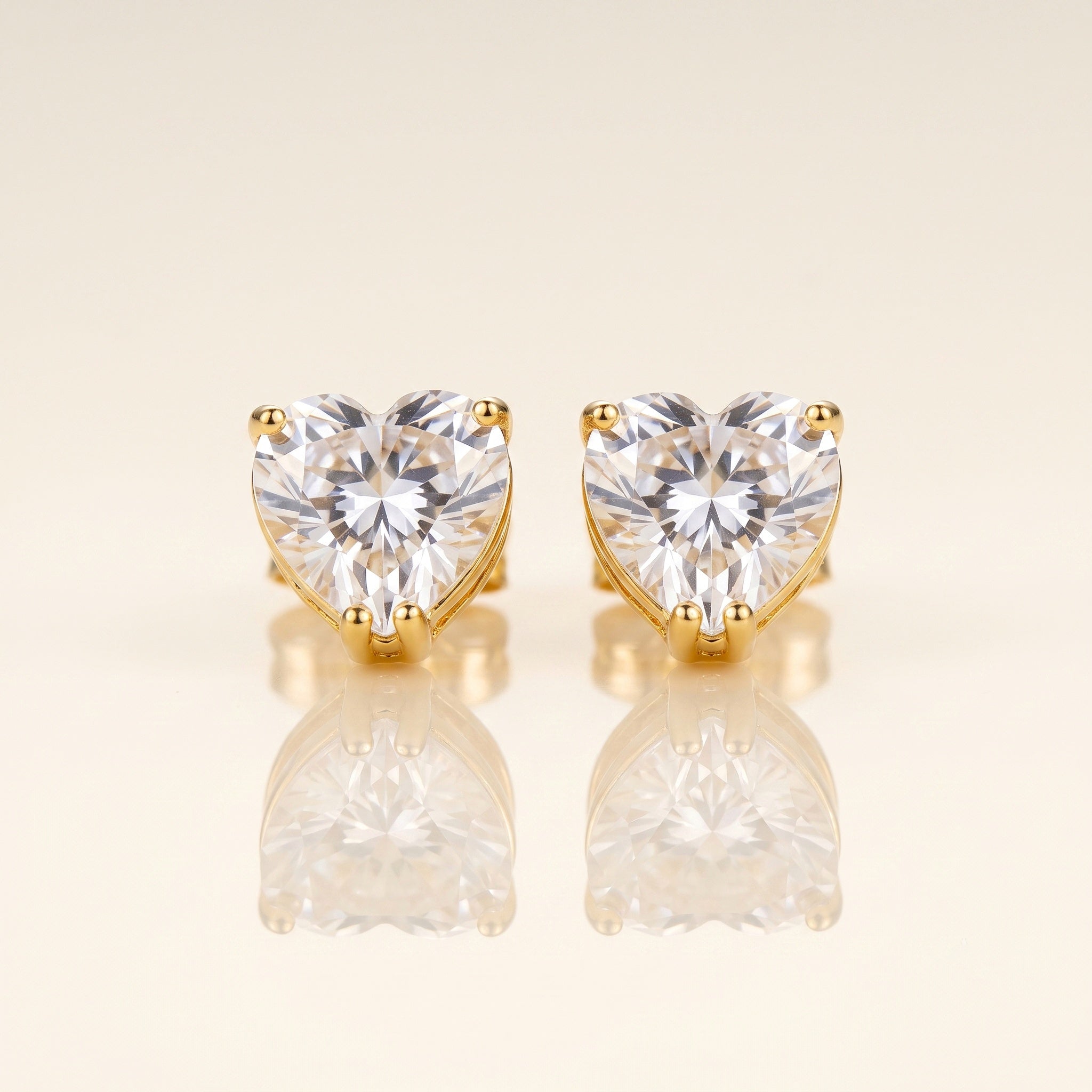 A pair of heart-shaped stud earrings with clear faceted gemstones in gold prong settings
