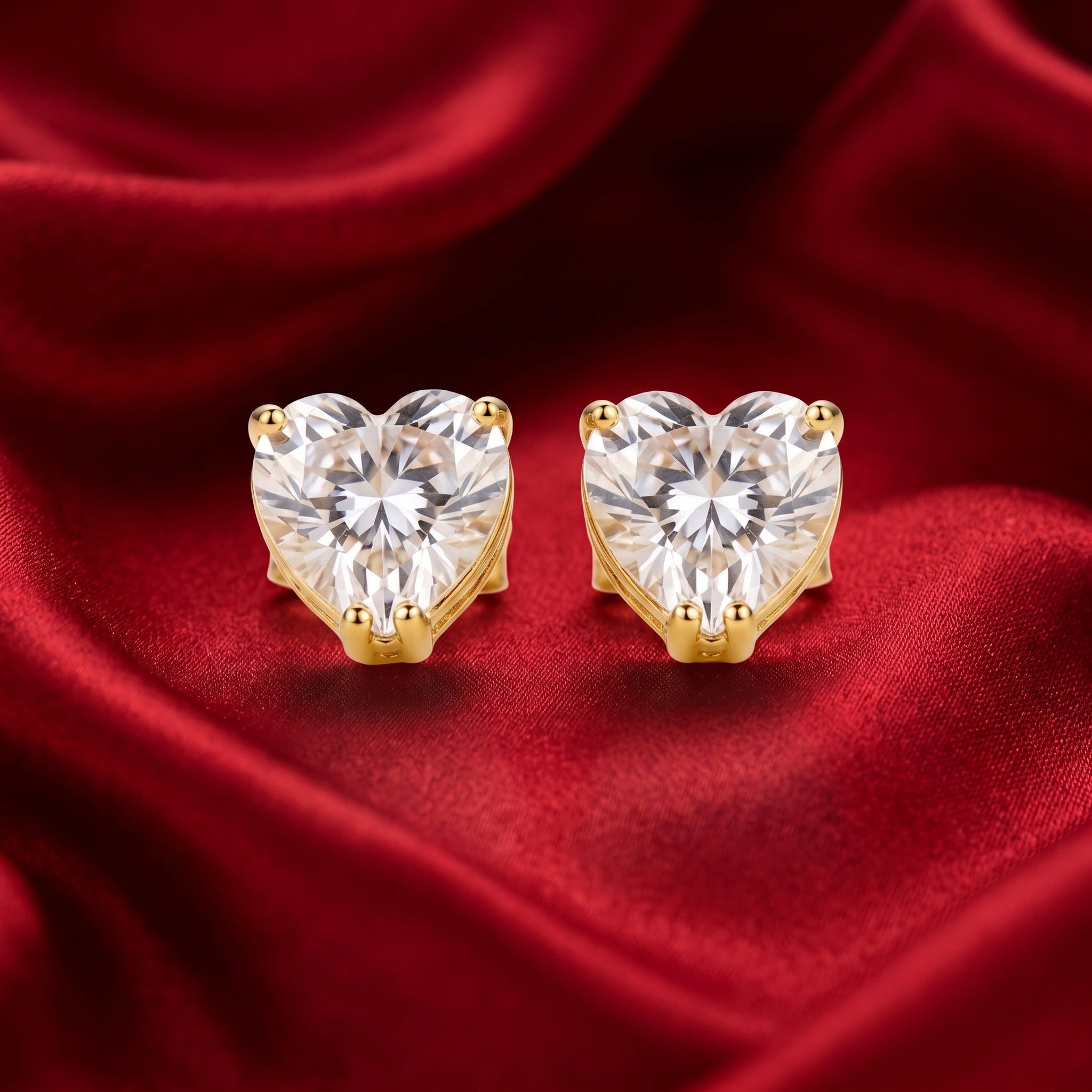 A pair of heart-shaped stud earrings with clear faceted gemstones in gold prong settings