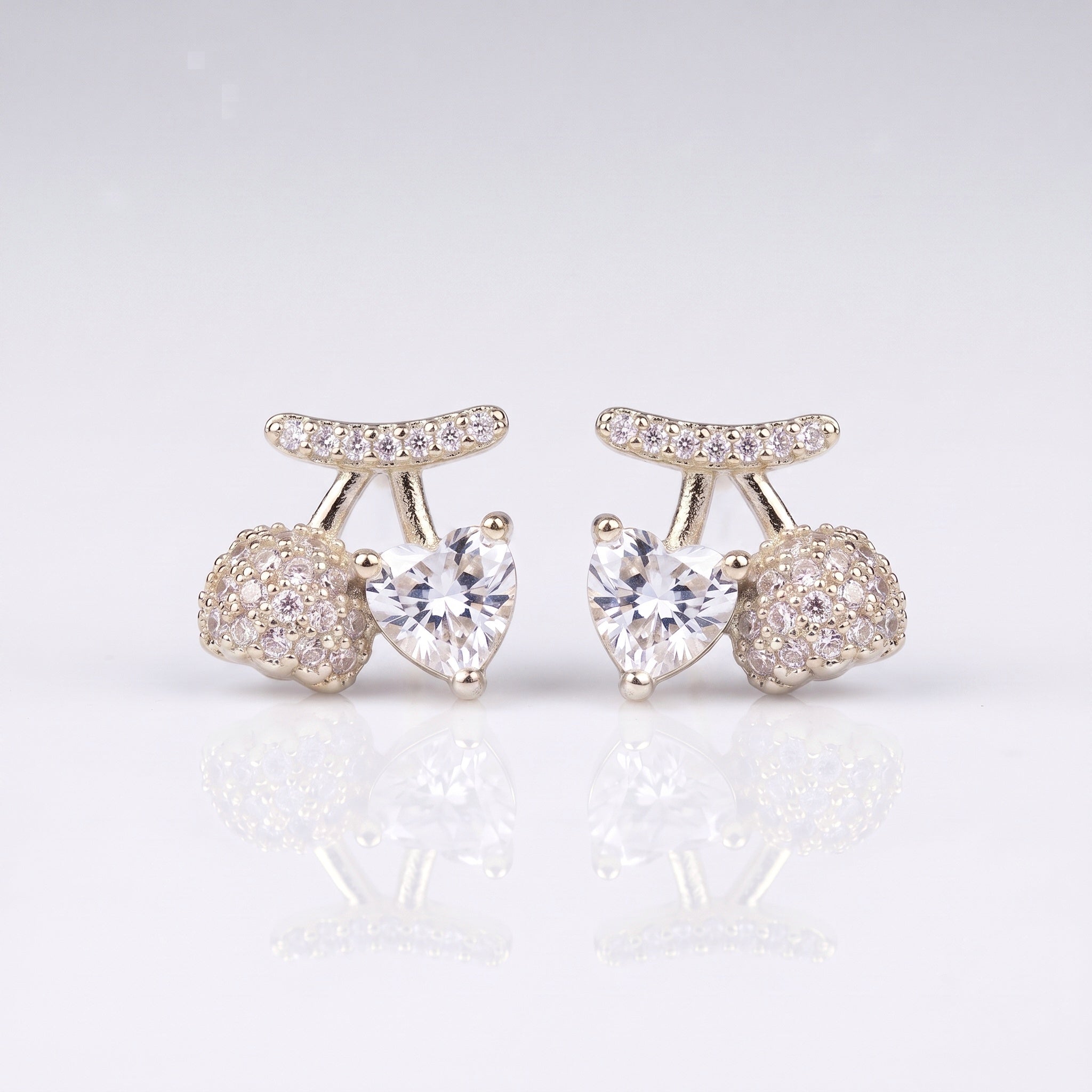 A pair of silver-toned stud earrings featuring a central heart-shaped clear gemstone, flanked by round pavé-set clear stones and a curved pavé top bar, 
