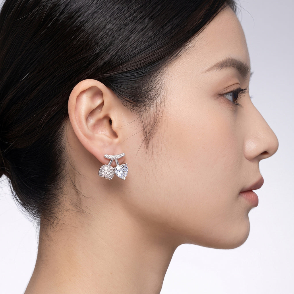 A pair of silver-toned stud earrings featuring a central heart-shaped clear gemstone, flanked by round pavé-set clear stones and a curved pavé top bar, 