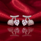A pair of silver-toned stud earrings featuring a central heart-shaped clear gemstone, flanked by round pavé-set clear stones and a curved pavé top bar