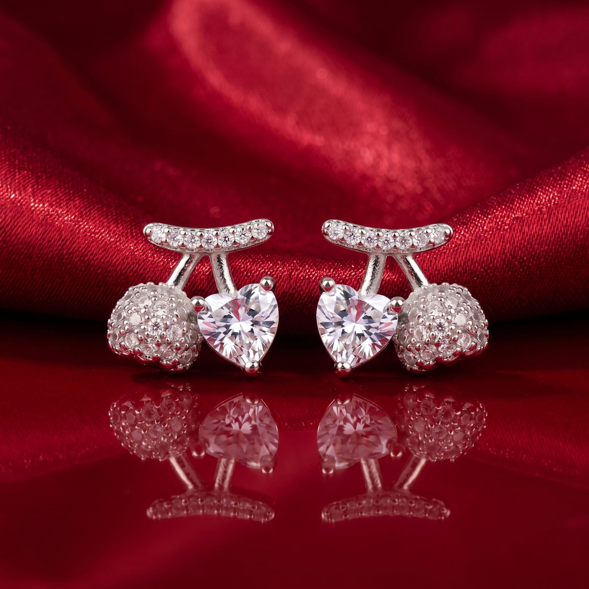 A pair of silver-toned stud earrings featuring a central heart-shaped clear gemstone, flanked by round pavé-set clear stones and a curved pavé top bar