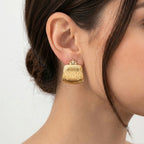A close-up of a model's ear wearing a A pair of gold clutch-style earrings with a crown-shaped top and a vertically ribbed, textured body