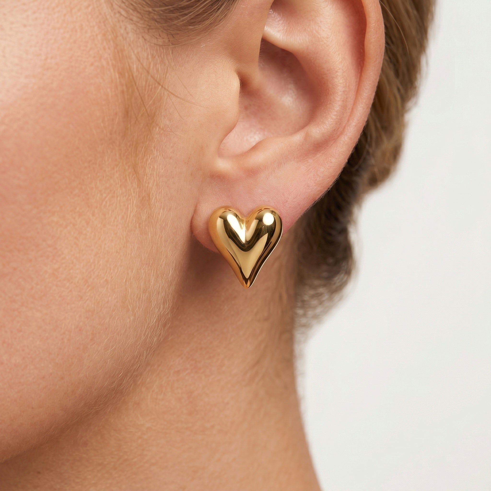 girl wearing a small, polished gold heart-shaped stud earring