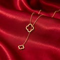 A delicate gold necklace with two interlocking clover-shaped pendants, displayed on a rich, draped red satin fabric.
