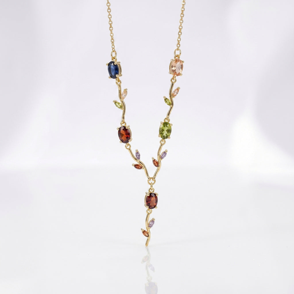 A delicate gold necklace featuring a vine-like pendant with multiple colorful gemstones in blue, green, red, and pink, displayed on a clean white background.