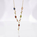 A delicate gold necklace featuring a vine-like pendant with multiple colorful gemstones in blue, green, red, and pink, displayed on a clean white background.