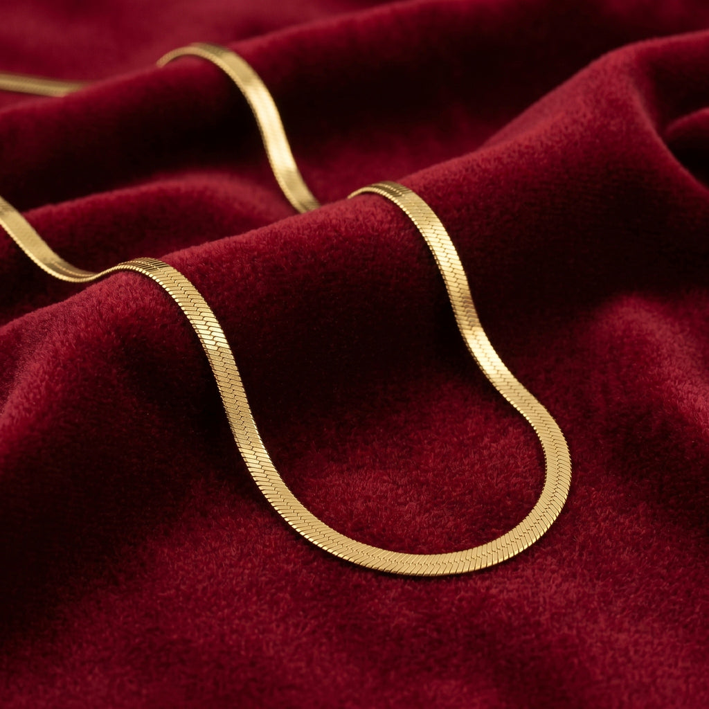 A close-up of a gold-toned chain necklace draped over rich burgundy velvet fabric.