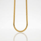 A gold snake chain necklace suspended in a U-shape against a clean white background with a soft reflection below.
