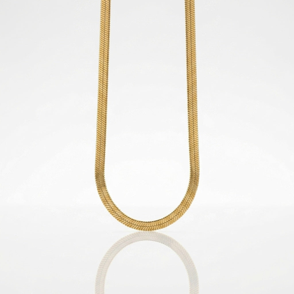 A gold snake chain necklace suspended in a U-shape against a clean white background with a soft reflection below.