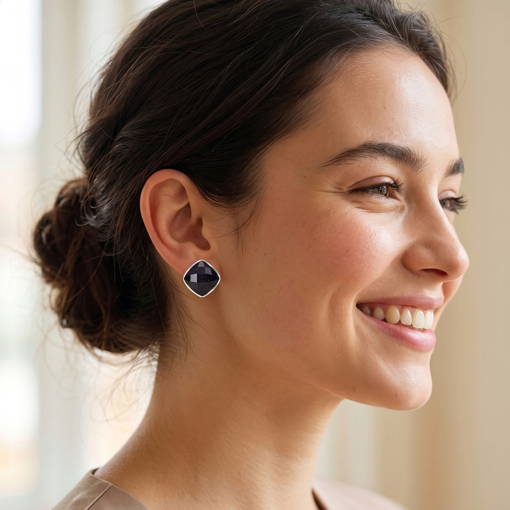 A woman with her hair in a low bun is shown in profile, wearing a small geometric stud earring with a dark blue-gray center and a silver-toned border.