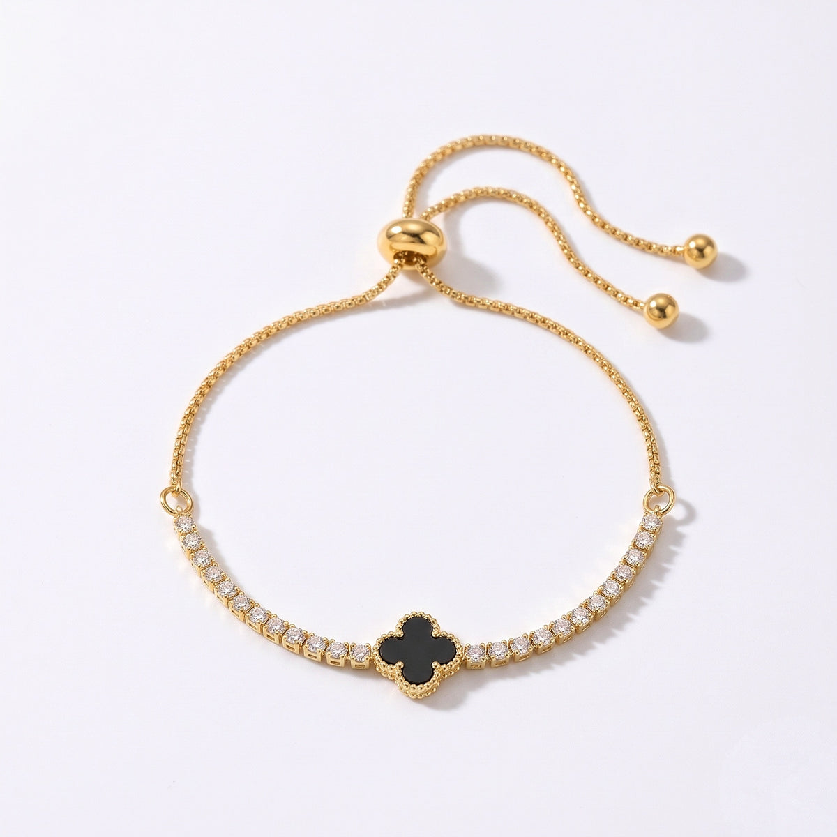 A gold-plated adjustable slide bracelet featuring a central black enamel four-leaf clover surrounded by small clear stones, set against a clean white background.