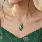 A close-up of a model wearing a silver chain necklace with a green bunny pendant adorned with sparkling clear stones. The model is wearing a green patterned top.