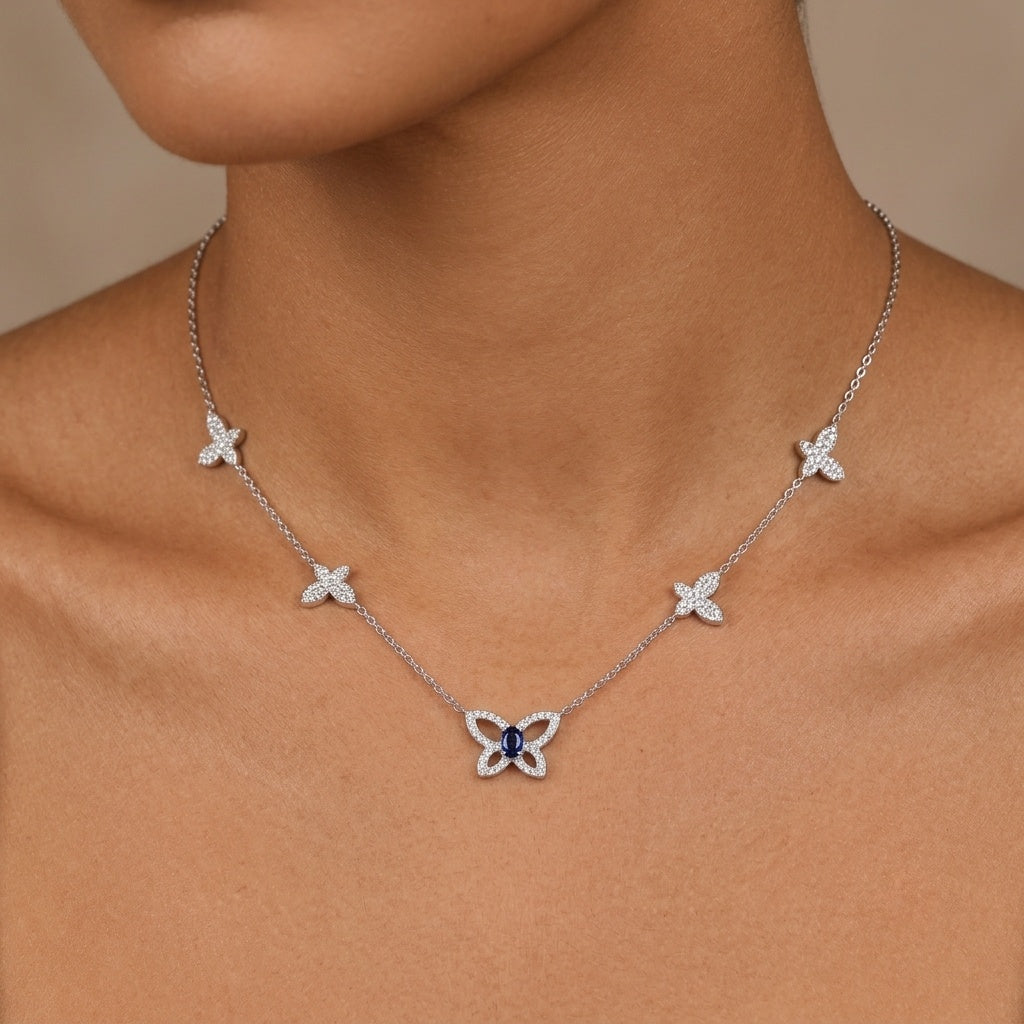 A close-up of a model wearing a delicate silver butterfly necklace. The necklace features a central silver butterfly pendant with a dark blue gemstone inlay, flanked by four smaller matching butterfly charms spaced along the chain.