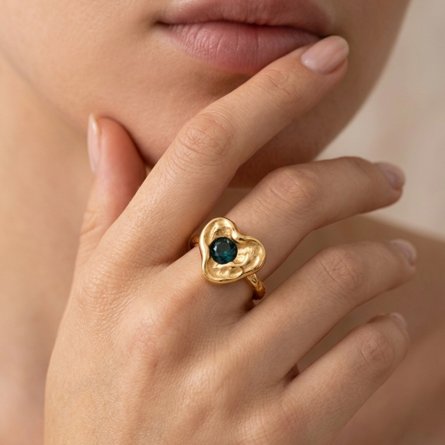 Gold heart-shaped ring with a green gemstone on a hand