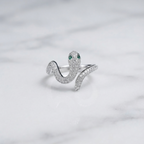 A silver snake ring paved with small clear stones, featuring green gemstone eyes, resting on a white marble surface.