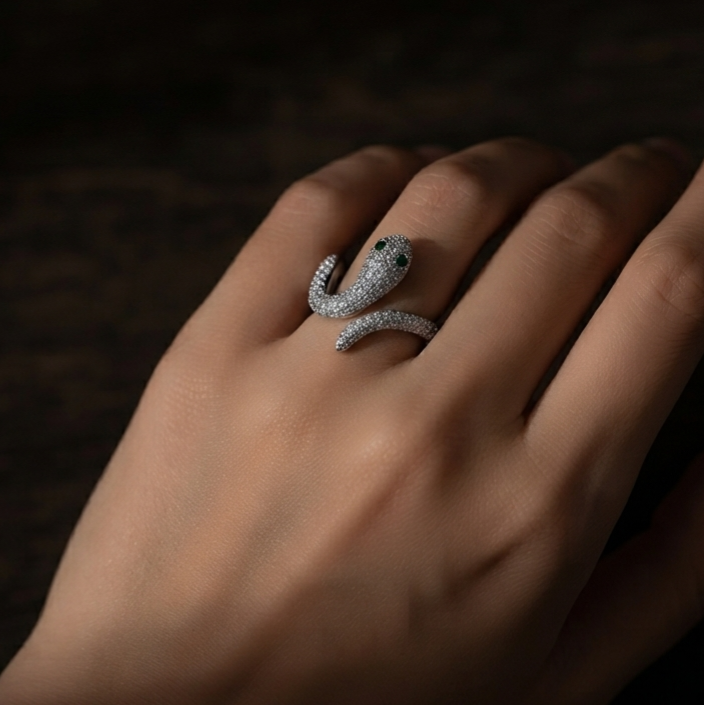 A silver snake-shaped ring with pavé-set stones worn on a hand, photographed against a dark, moody background.