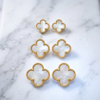 Six gold-tone four-leaf clover stud earrings with white mother-of-pearl inlays, arranged on a white marble surface.
