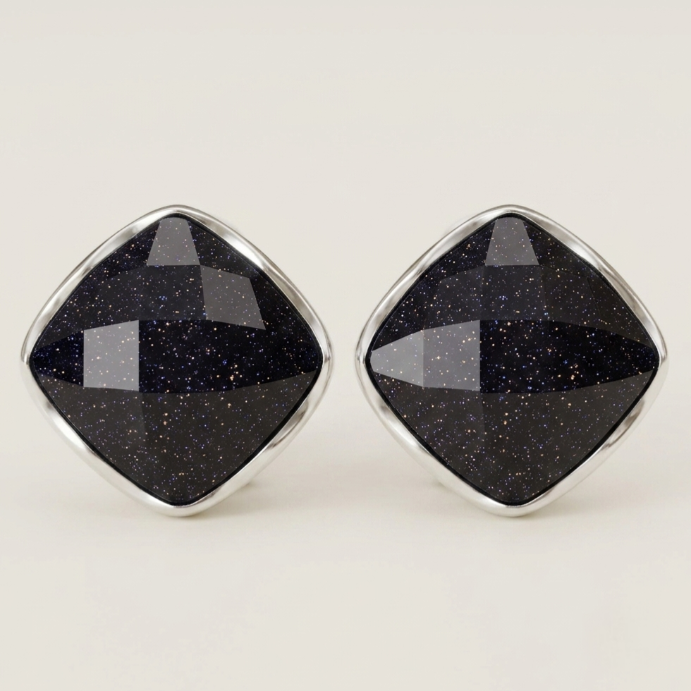 A pair of diamond-shaped stud earrings featuring faceted black stone with subtle gold speckles, set in polished silver-tone metal bezels, on a light cream background.