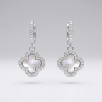 A pair of silver-toned dangle earrings featuring a clover motif with a white mother-of-pearl center and a border of small clear pavé stones, shown on a neutral light gray background.