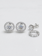 Silver-tone stud earrings with round-cut clear center stones surrounded by a halo of smaller clear stones, shown on a clean white background with one earring displayed front-on and another showing the side/back detail.