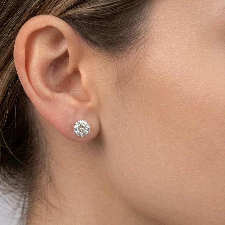 A close-up of a person's ear wearing a single round brilliant-cut diamond stud earring in a silver setting.