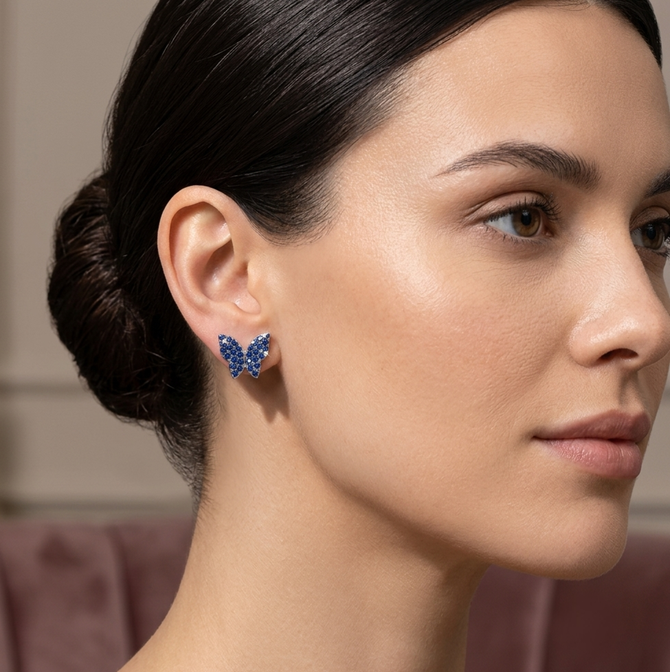 A close-up side profile of a woman with dark hair in a bun, wearing a small butterfly-shaped stud earring set with sparkling blue stones.