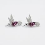 A pair of silver-toned bird stud earrings with sparkling clear stones and a central teardrop-shaped pink gemstone, displayed on a clean white background.