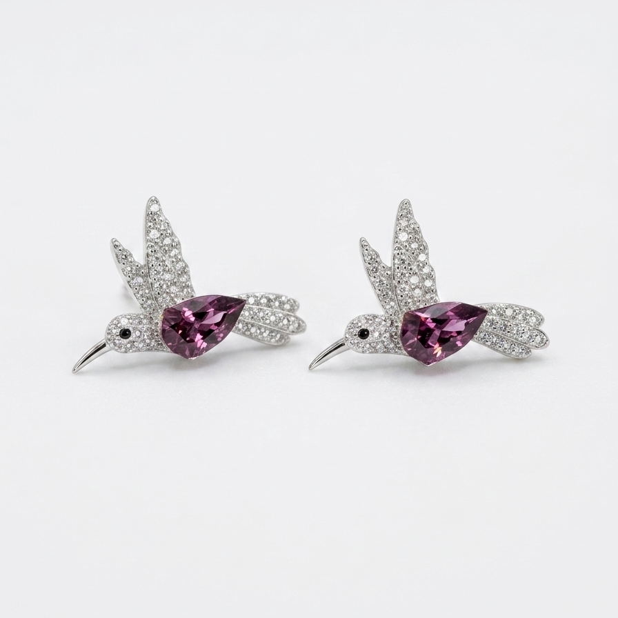A pair of silver-toned bird stud earrings with sparkling clear stones and a central teardrop-shaped pink gemstone, displayed on a clean white background.