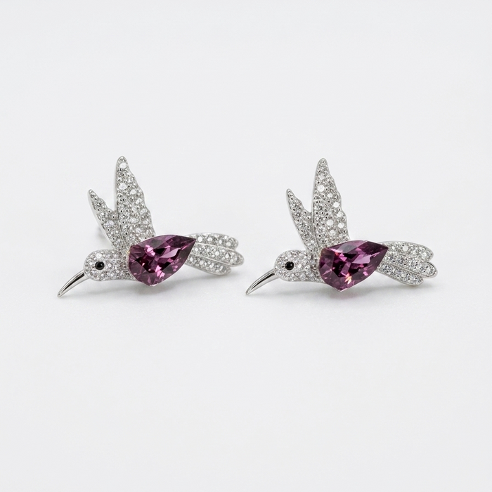 A pair of silver-toned bird stud earrings with sparkling clear stones and a central teardrop-shaped pink gemstone, displayed on a clean white background.