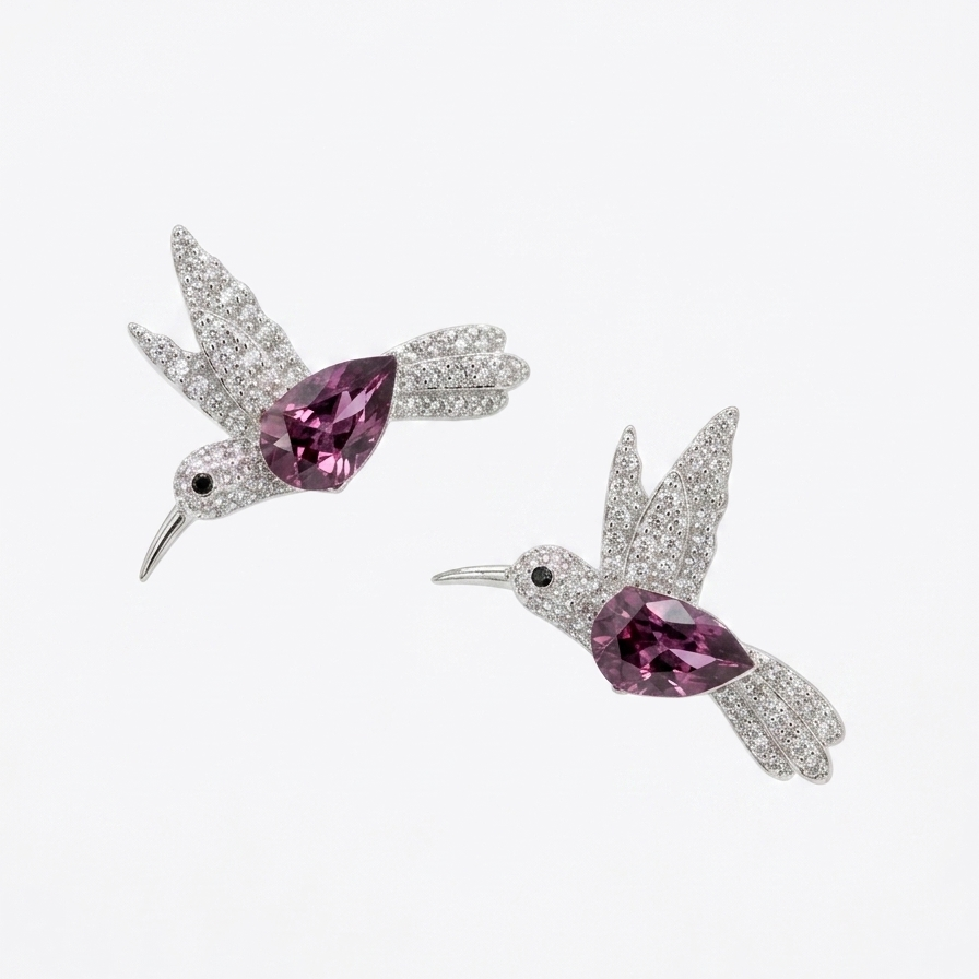 A pair of silver-toned hummingbird stud earrings paved with clear stones, featuring a central marquise-cut pink gemstone, shown on a plain white background.