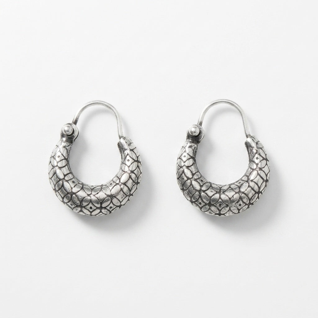 A pair of textured silver crescent hoop earrings with a raised, patterned surface and fishhook backings, displayed on a clean white background.
