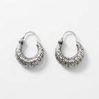 A pair of textured silver crescent hoop earrings with a raised, patterned surface and fishhook backings, displayed on a clean white background.