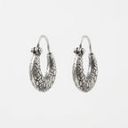 A pair of textured silver hoop earrings with a hammered, organic pattern, shown against a plain light gray background.