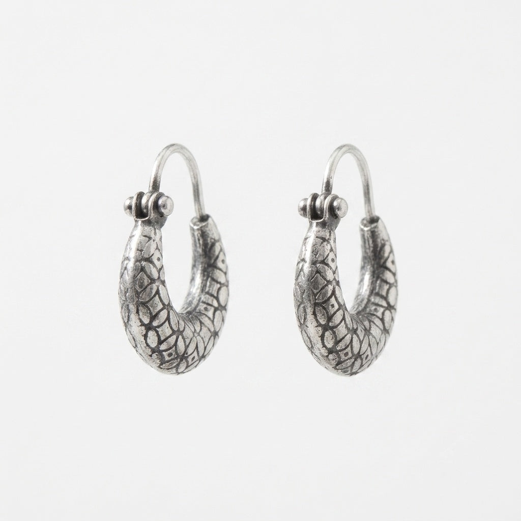 A pair of textured silver hoop earrings with a hammered, organic pattern, shown against a plain light gray background.