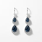 A pair of silver drop earrings featuring pear-shaped dark blue gemstones surrounded by small clear stones, shown on a clean white background.