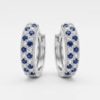 A pair of silver huggie hoop earrings adorned with rows of round-cut blue sapphires and clear pavé diamonds, set against a clean white background.