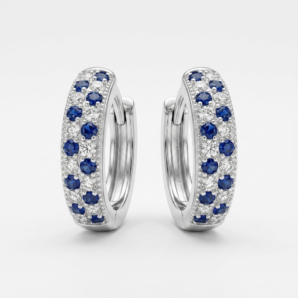 A pair of silver huggie hoop earrings adorned with rows of round-cut blue sapphires and clear pavé diamonds, set against a clean white background.